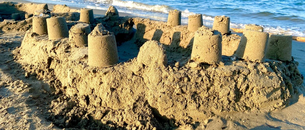 Auf einem Strand ist eine große Sandburg vor dem Meer zu sehen.